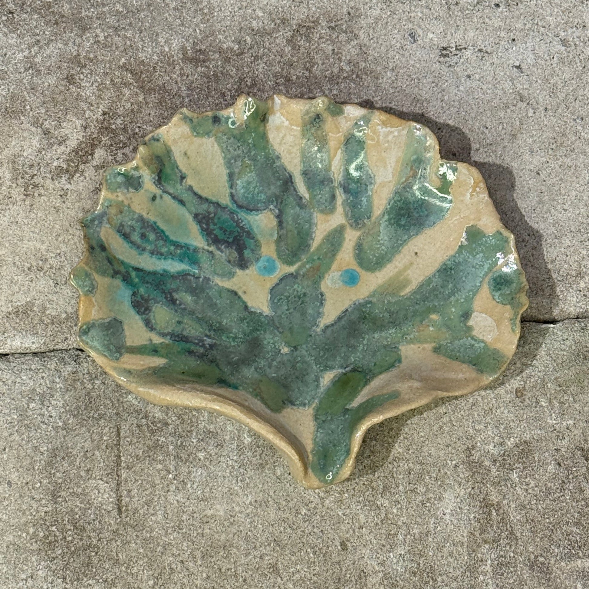 Decorative seashell ceramic plate with green and beige patterns on a concrete surface