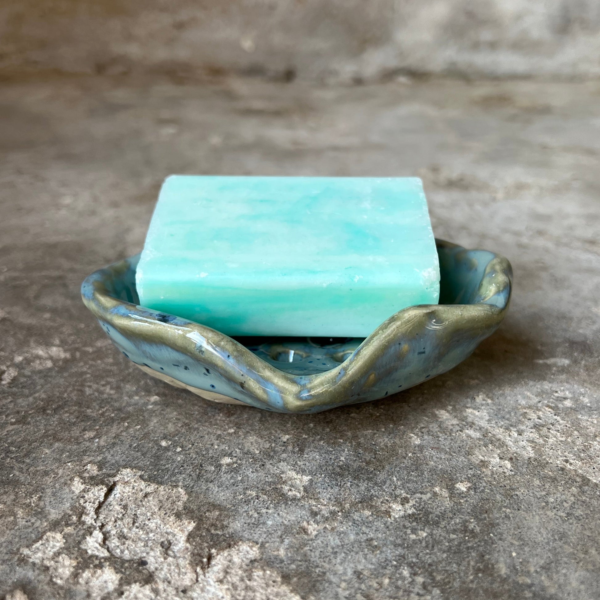Turquoise soap bar with a decorative seashell holder on a textured stone surface