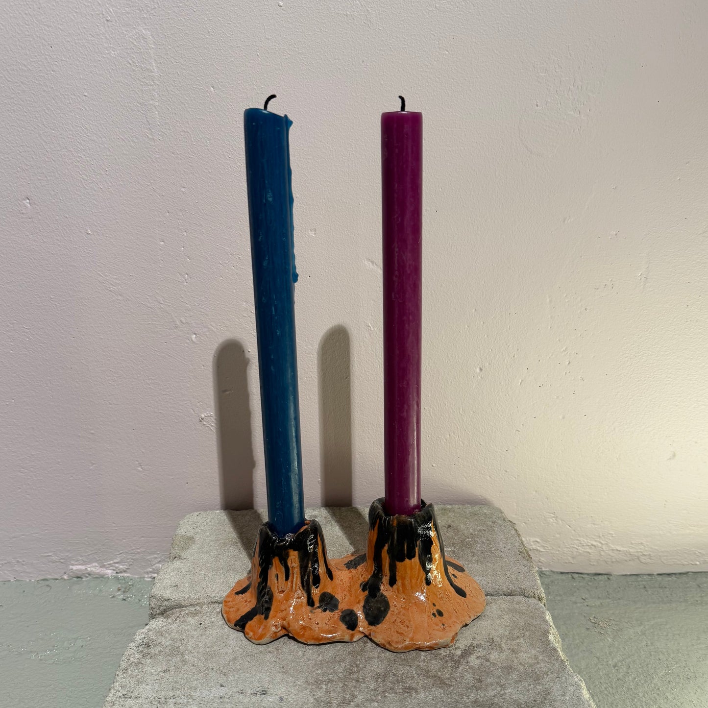 Two candles, one blue and one purple, in a decorative ceramic candle holder against a plain wall.