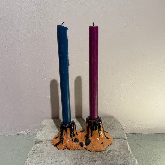 Two candles, one blue and one purple, in a decorative ceramic candle holder against a plain wall.