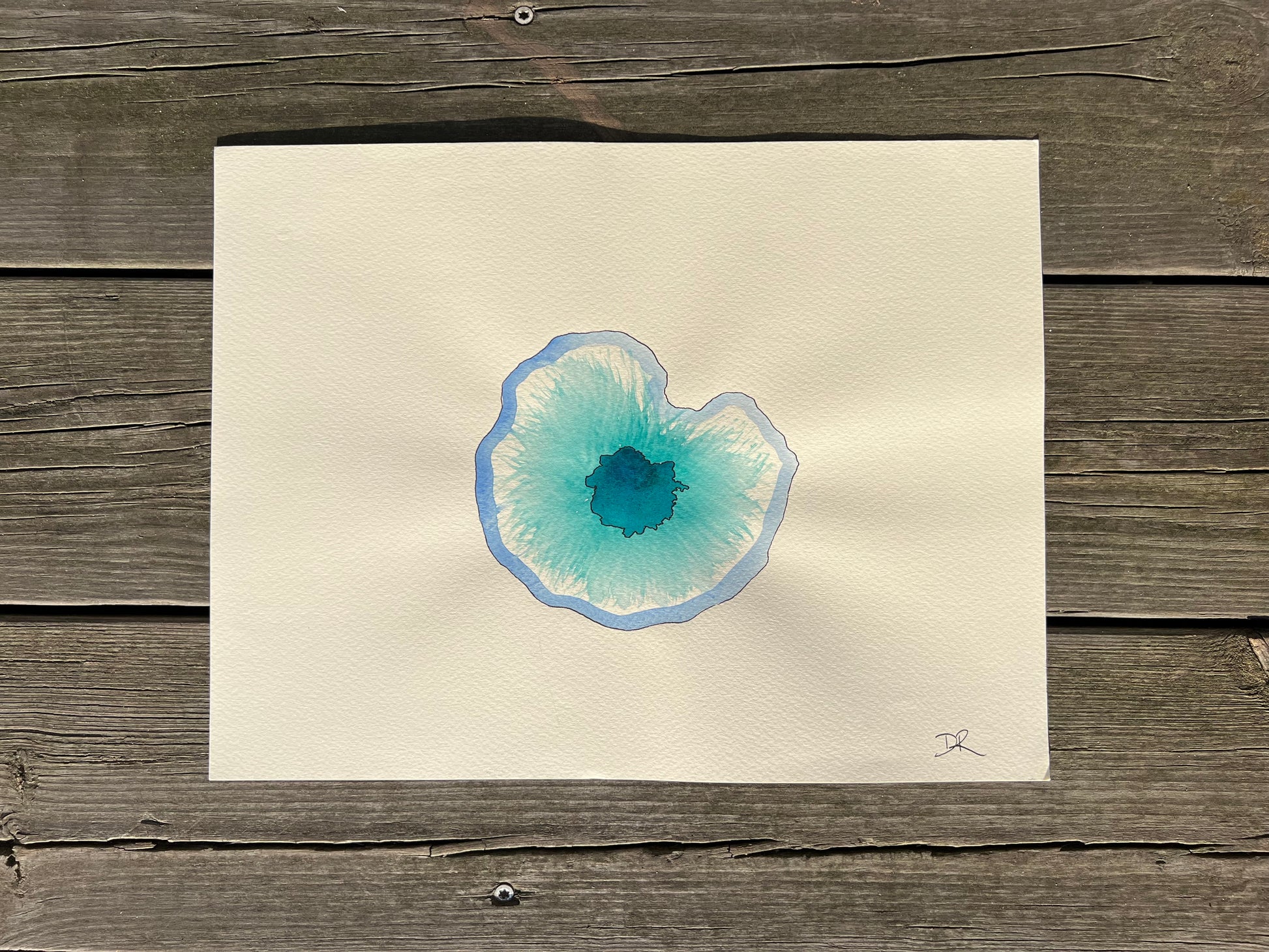 Artistic depiction of a blue and green eye in watercolor on beige paper, placed on a wooden surface.