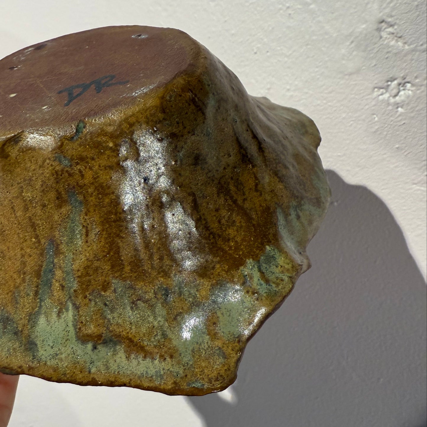 Hand holding a piece of greenish-brown ceramic bowl against a white background