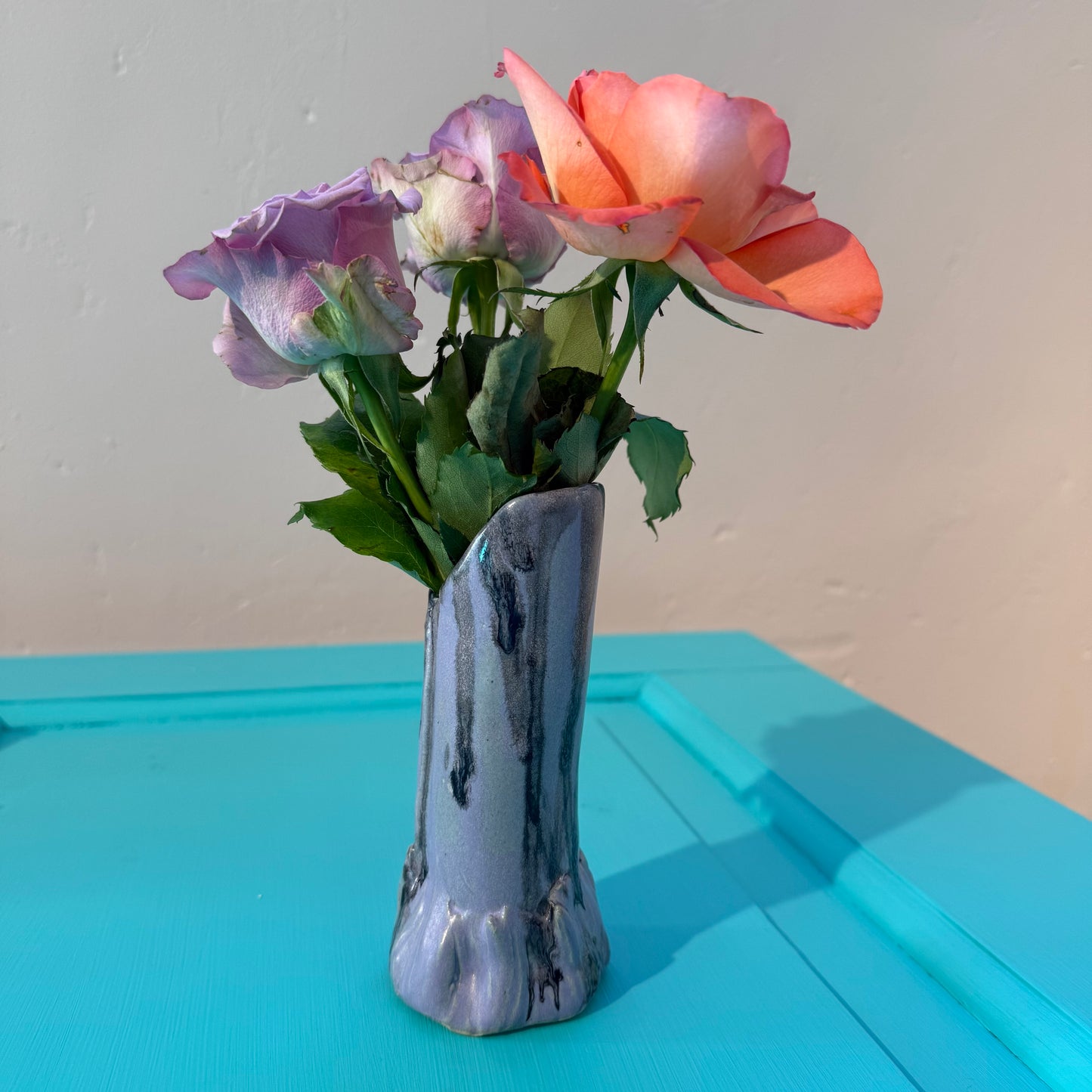 Vase with flowers on a light blue surface against a plain background