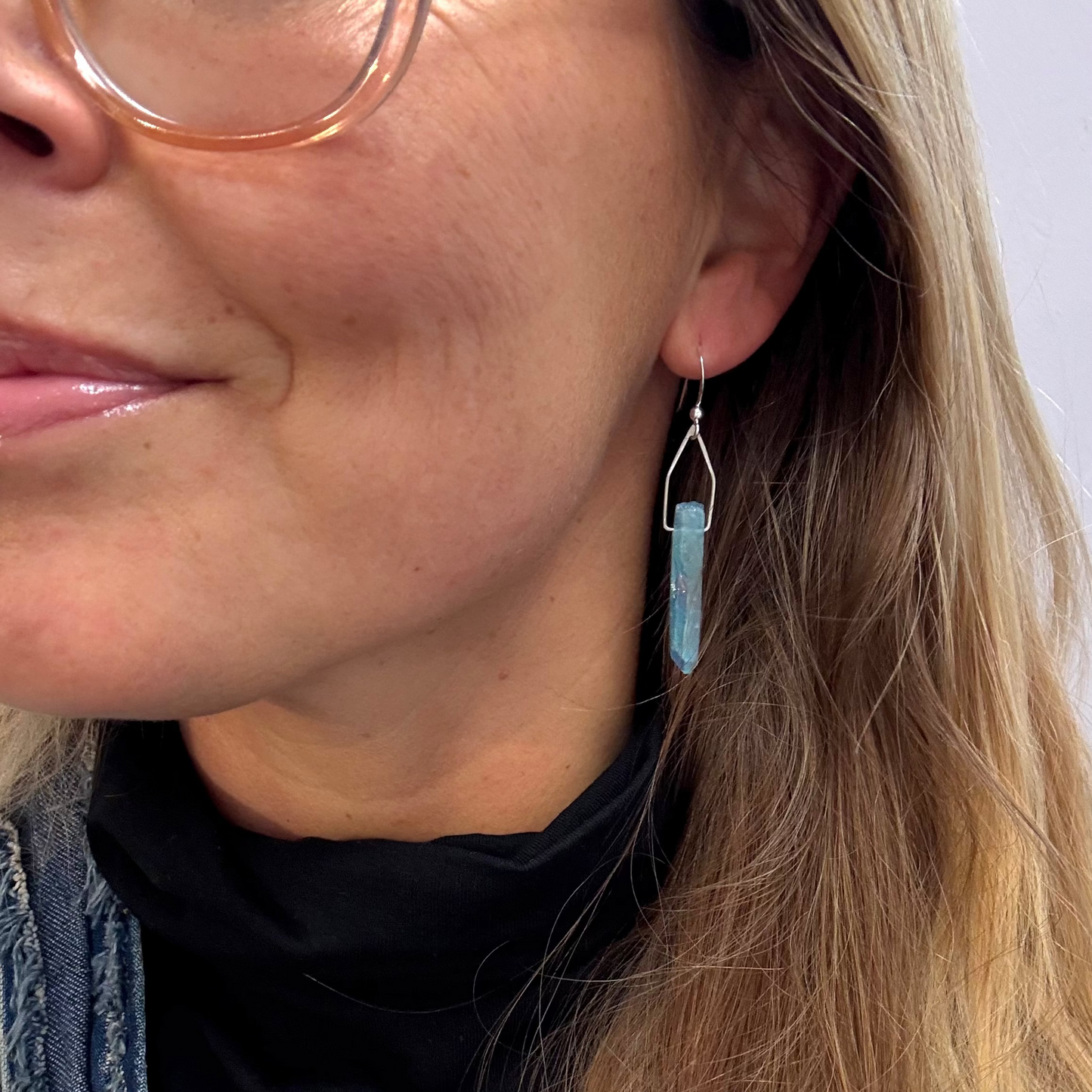 Close-up of a person wearing a blue crystal earring with a soft pink background