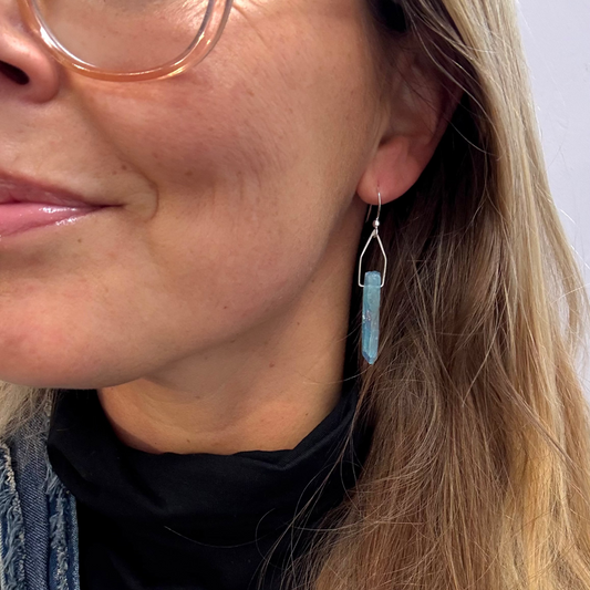 Close-up of a person wearing a blue crystal earring with a soft pink background