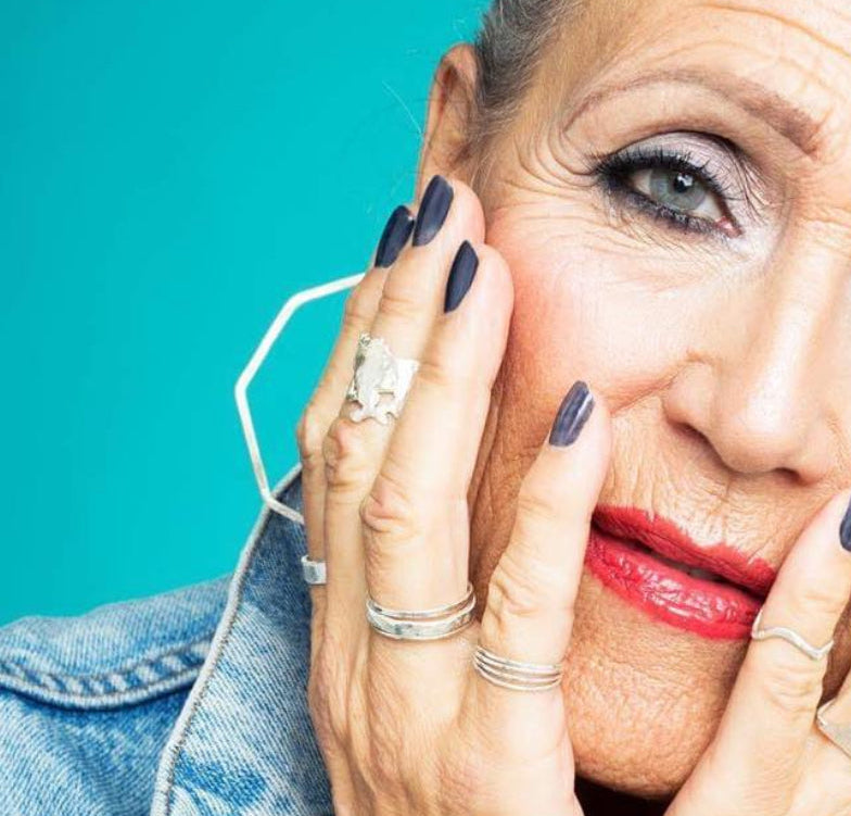 Woman with gray hair and blue denim jacket against a teal background