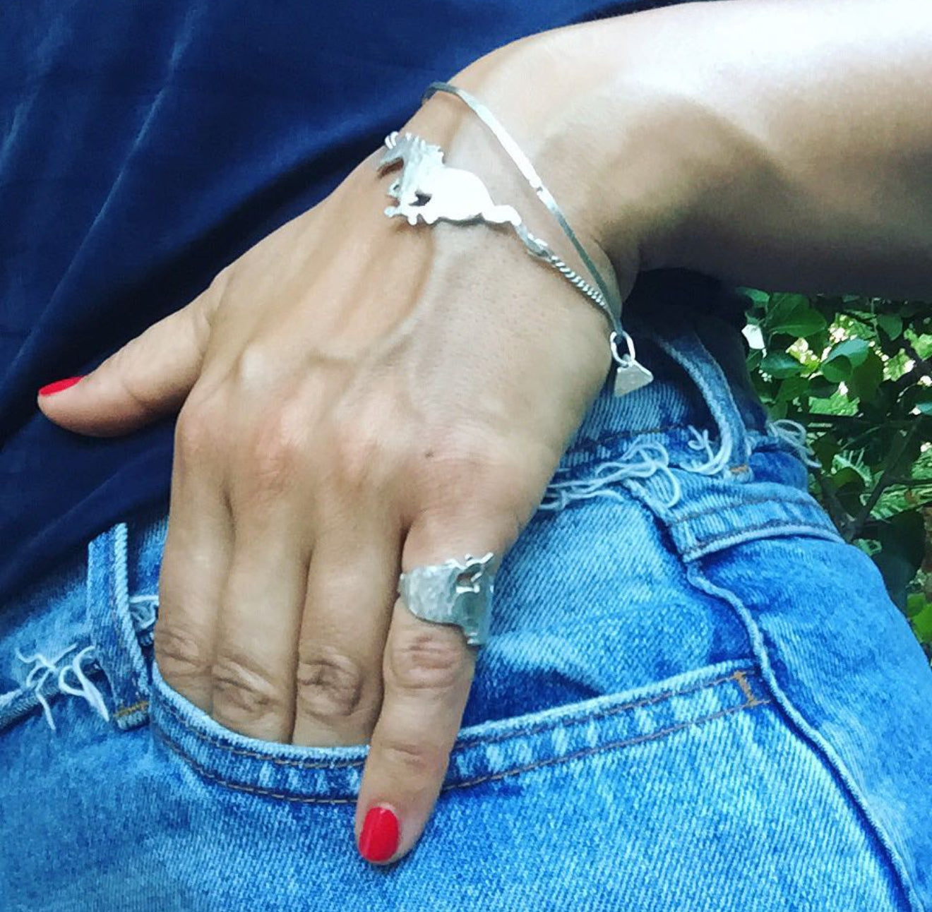 Hand wearing silver rings and a bracelet with horse design on a blue denim background