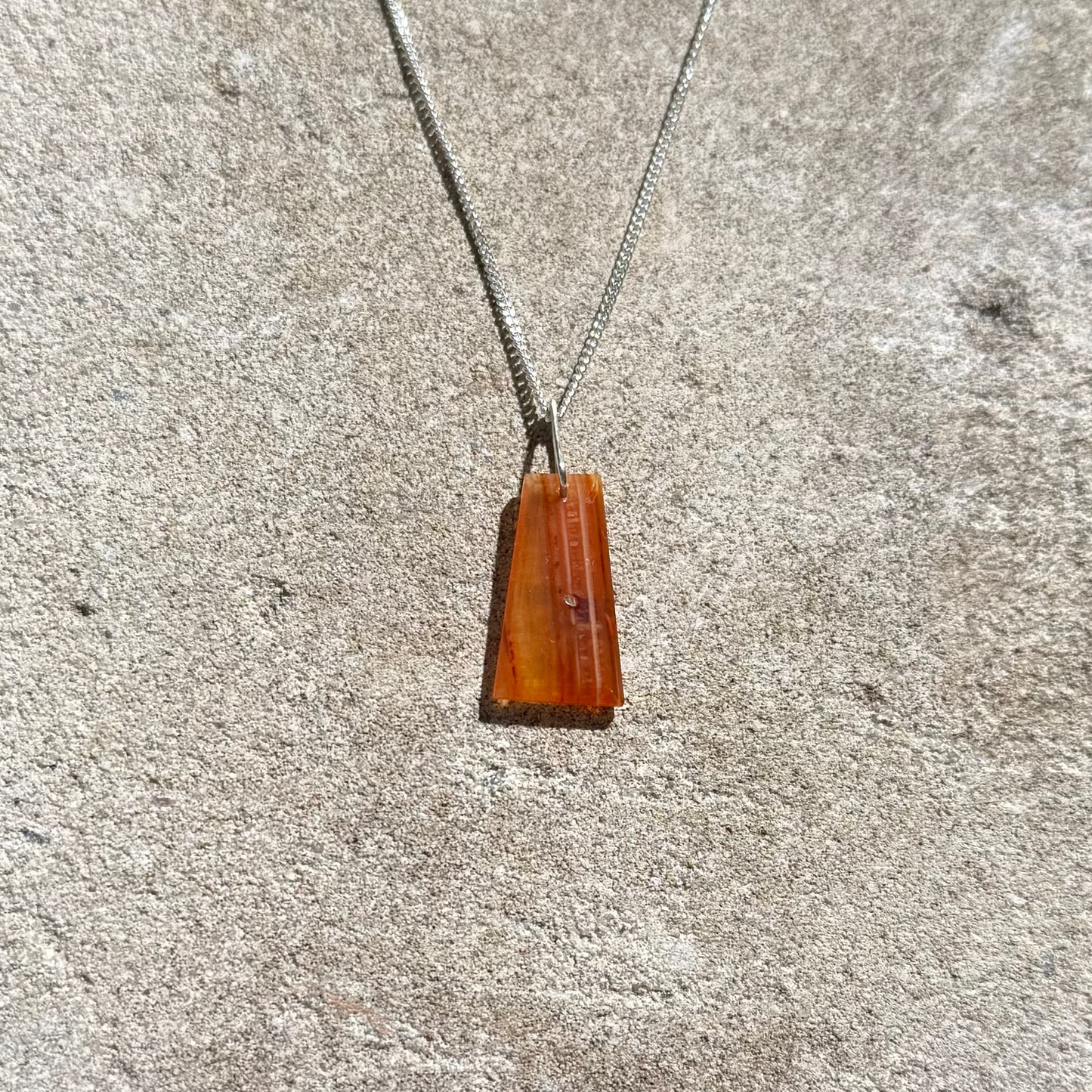 orange crystal silver necklace on a textured stone surface