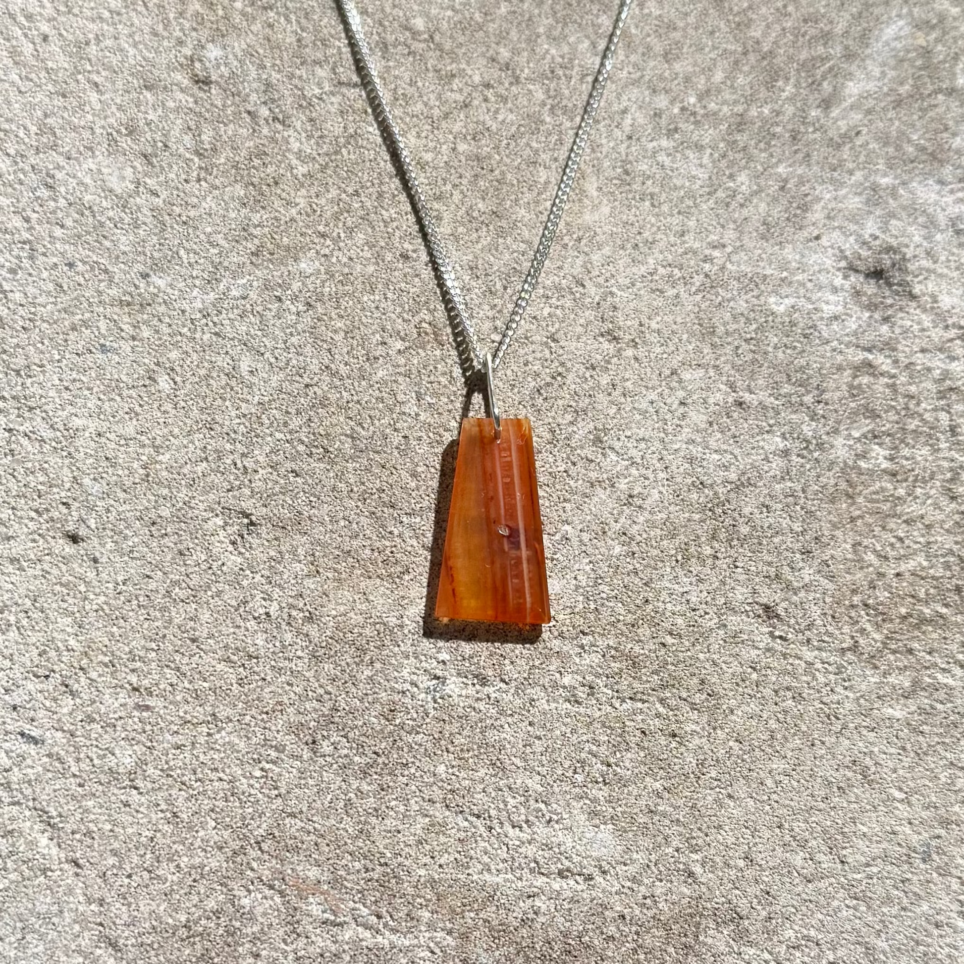 orange crystal silver necklace on a textured stone surface
