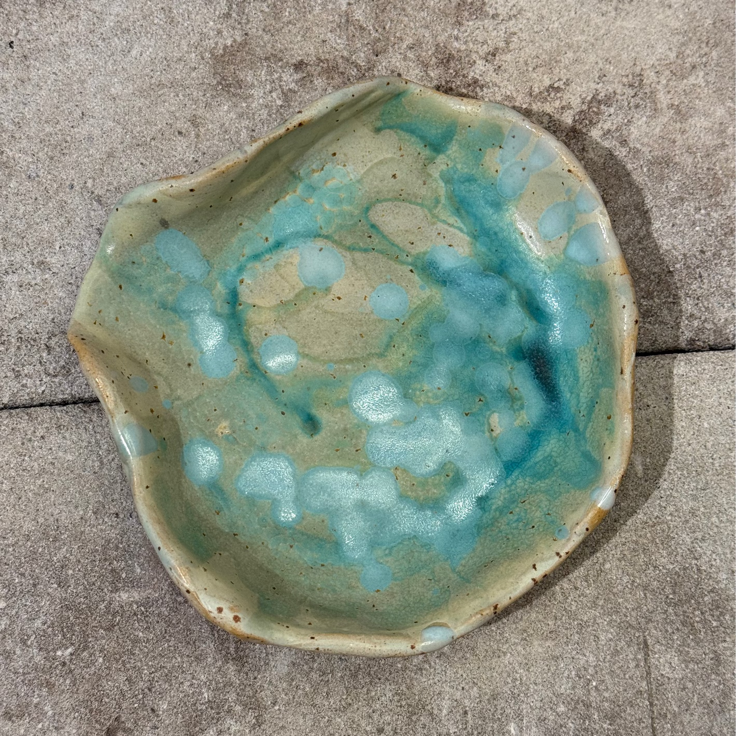 Ceramic seashell-shaped dish with blue and green glaze on a concrete surface