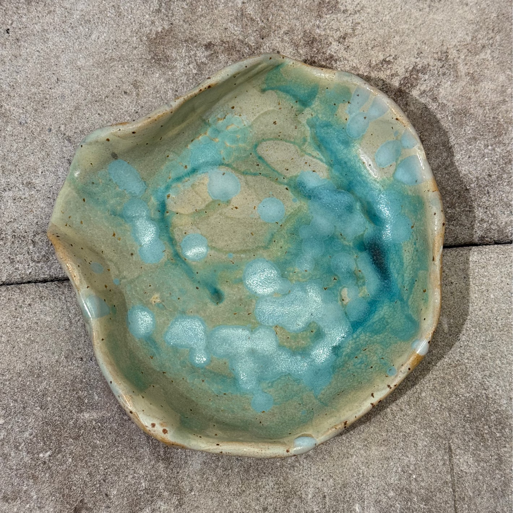Ceramic seashell-shaped dish with blue and green glaze on a concrete surface