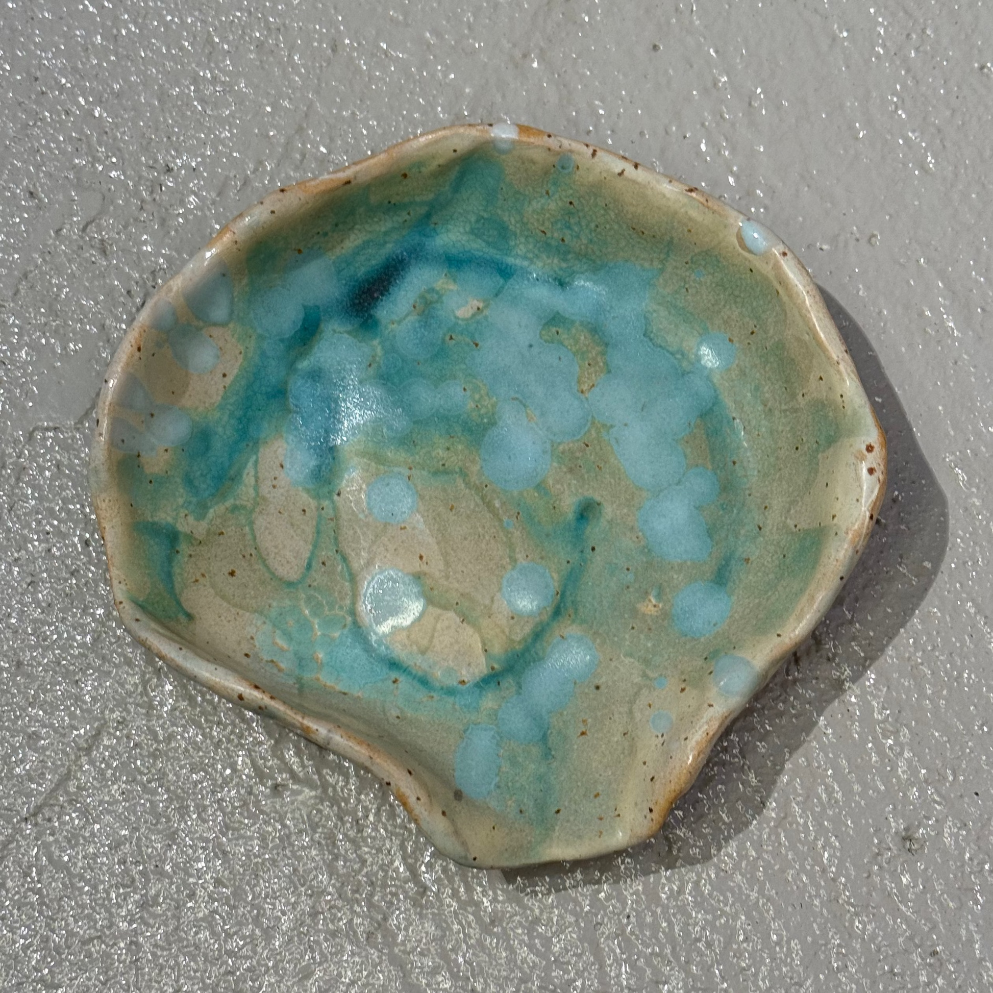 Ceramic seashell dish with blue glaze on a sandy surface