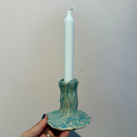 candle holder in ceramics with matte teal glazing and white candle on a soft pink background