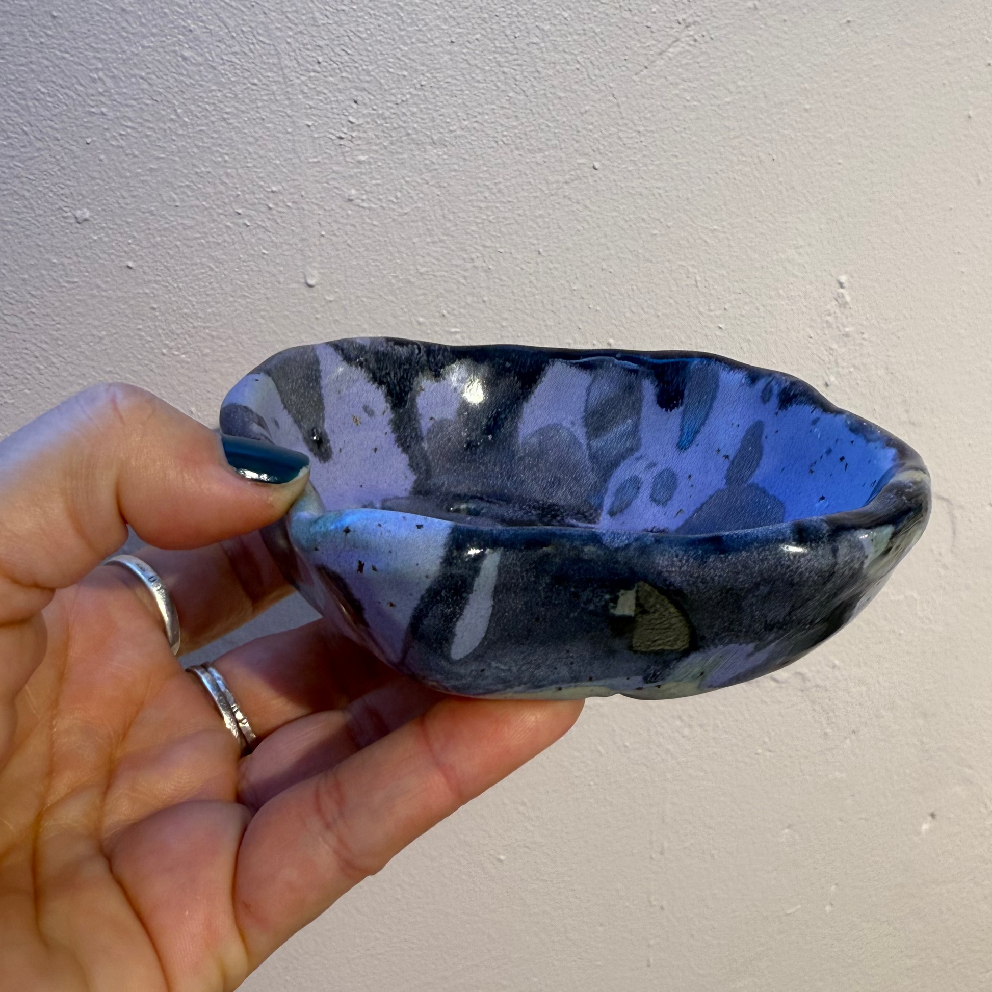 Hand holding a purple and black ceramic soap dish against a plain background