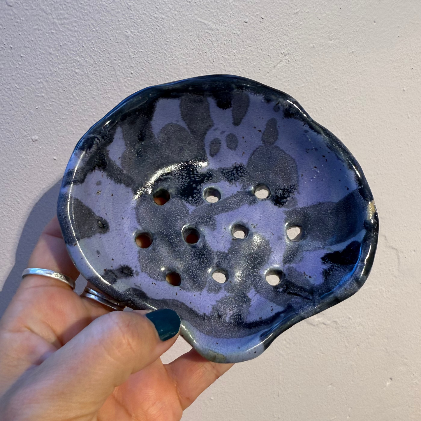 Hand holding a purple and black ceramic soap dish against a plain background