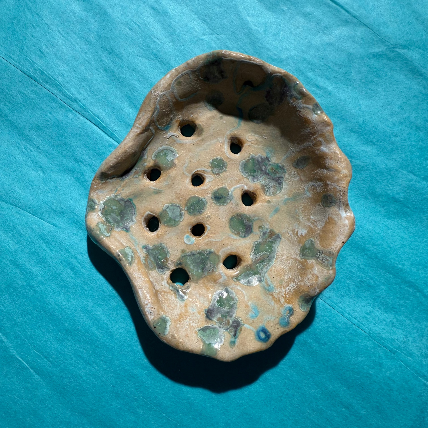Ceramic soap dish with green speckles on a blue surface